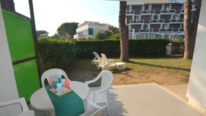 A patio area with a table and chairs, a small table with a tray of items, and a view of a building in the background. - Pretty Villa Ideal for Families in Lignano Sabbiadoro (Lignano Sabbiadoro)