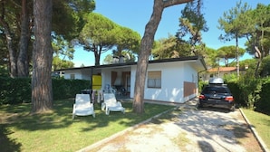A two-story house with a covered porch, a car parked in front, and a lawn with chairs. - Pretty Villa Ideal for Families in Lignano Sabbiadoro (Lignano Sabbiadoro)