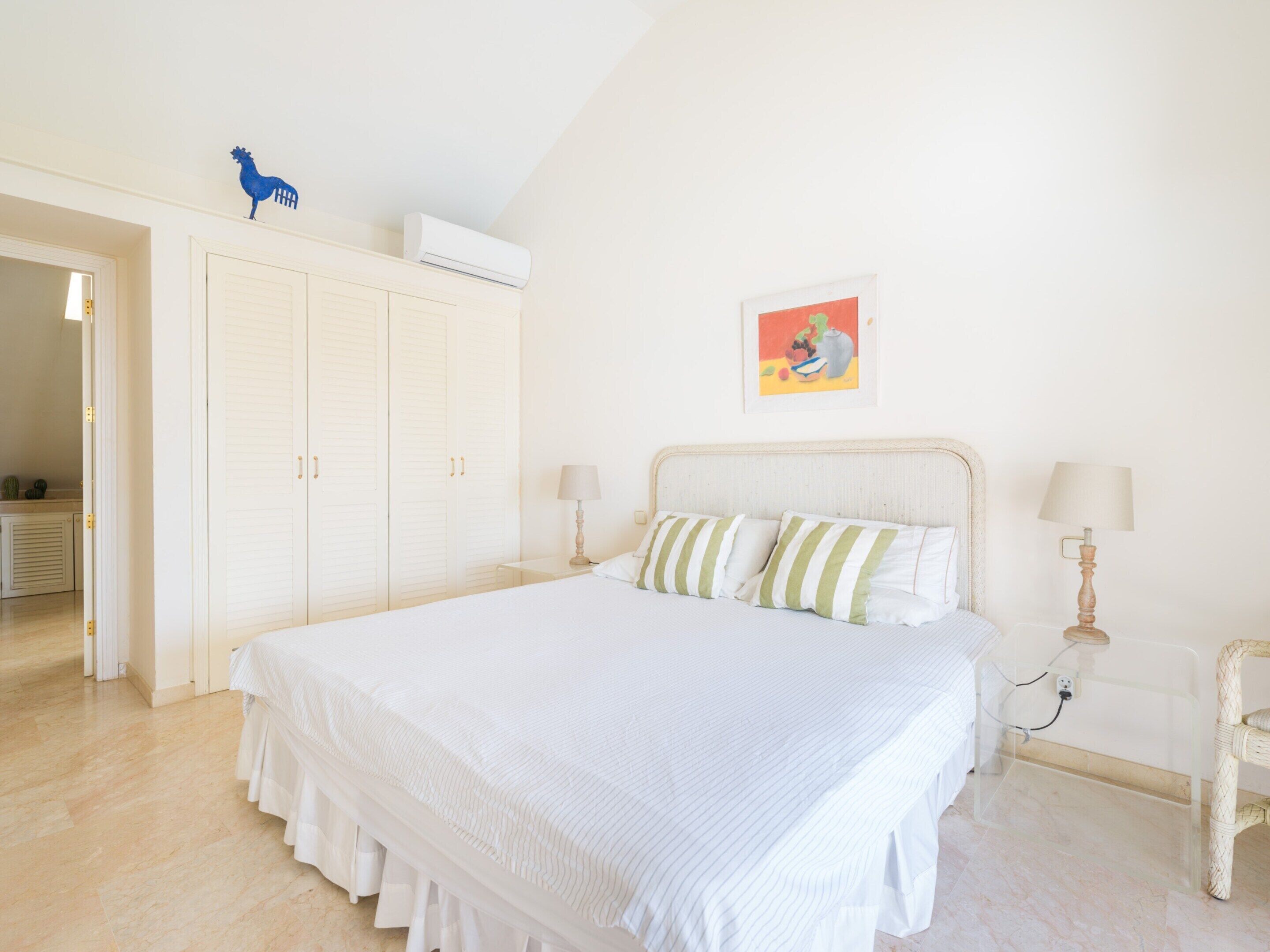A bedroom with a large bed, white walls, a ceiling fan, and a door leading to another room.