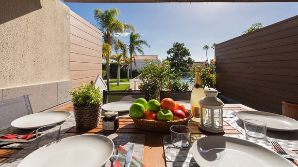 An outdoor dining area with a table set for two, featuring a fruit basket, a bottle, and a lantern.