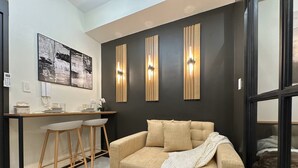 A modern living room with a sofa, a coffee table, and a desk with two chairs. There are wall-mounted light fixtures and framed artwork on the wall. - Premium Suites City View, Makati CBD, Netflix, Wi-Fi & 20 mins to Airport (Makati)