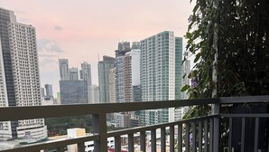 A balcony with a wooden table, two cushioned chairs, a potted plant, and a book titled "VOULPE". - Premium Suites City View, Makati CBD, Netflix, Wi-Fi & 20 mins to Airport (Makati)