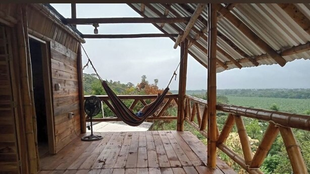 Una terraza de madera con una hamaca y un ventilador, con vistas a un paisaje exuberante.