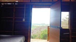 Una habitación con una cama, una puerta de madera y vistas a un paisaje verde.