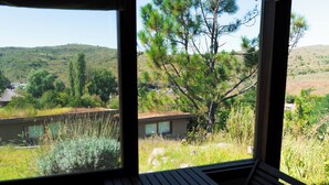 A room with a large window overlooking a grassy area with trees and a hill.