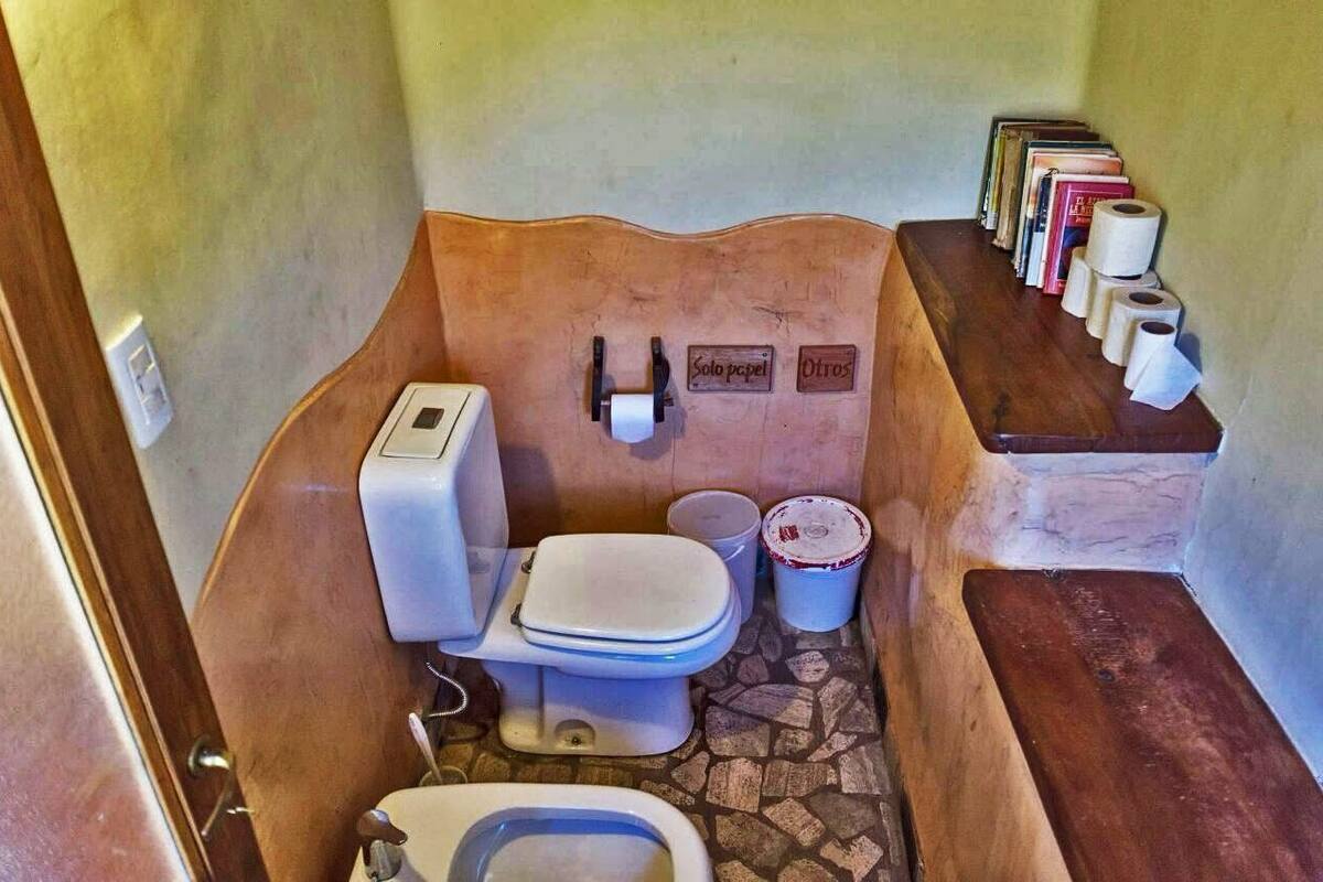 Un baño con inodoro, bidé y estante con libros y papel higiénico.