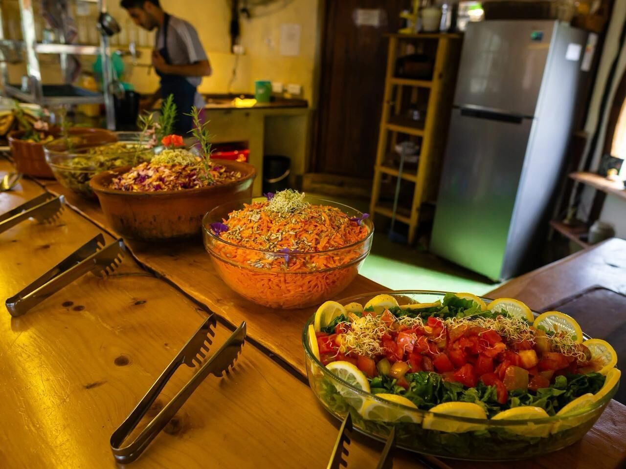 Una mesa de buffet con diversos platos, incluyendo una ensalada y un guiso de verduras, en una cocina.
