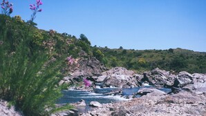 A rocky shoreline with clear blue water, surrounded by greenery and hills.