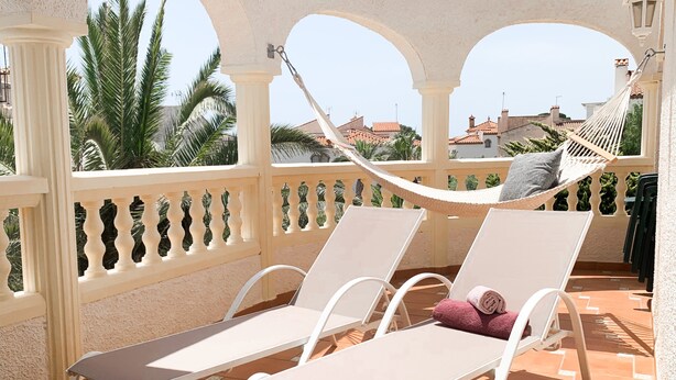 A terrace with two white lounge chairs, a hammock, and a view of palm trees and buildings. - Poolvilla Michelle near the beach (Mont-roig del Camp)