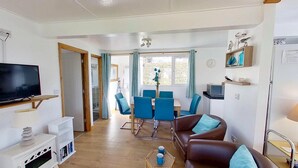 A living room with a TV, sofa, and dining area with chairs. - D48 Sunvale, Riviere Towans (Hayle)