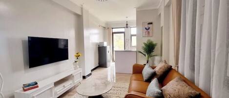 A modern living room with a flat-screen TV, a white console table, a patterned rug, and a brown sofa with cushions.