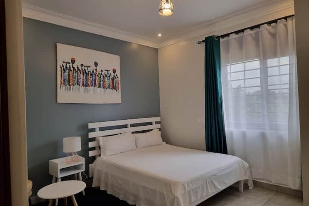 A bedroom with a bed, a bedside table with a lamp, a small round table, and a wall-mounted artwork.