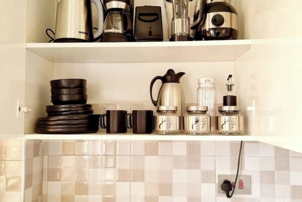 Une étagère de cuisine contenant divers appareils pour préparer le café, notamment une machine à café, un moulin et plusieurs tasses.