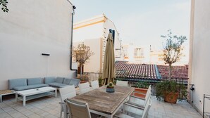 An outdoor patio with a wooden table, white chairs, a grey sofa, and a potted plant. - Casa Santa Sofia con Terrazza by Wonderful Italy (Palermo)