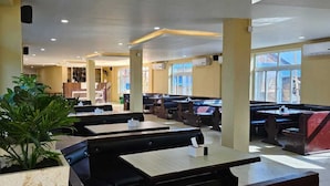 Ein Restaurant mit mehreren Tischen und Sitzecken, großen Fenstern und einem Topfpflanzen.