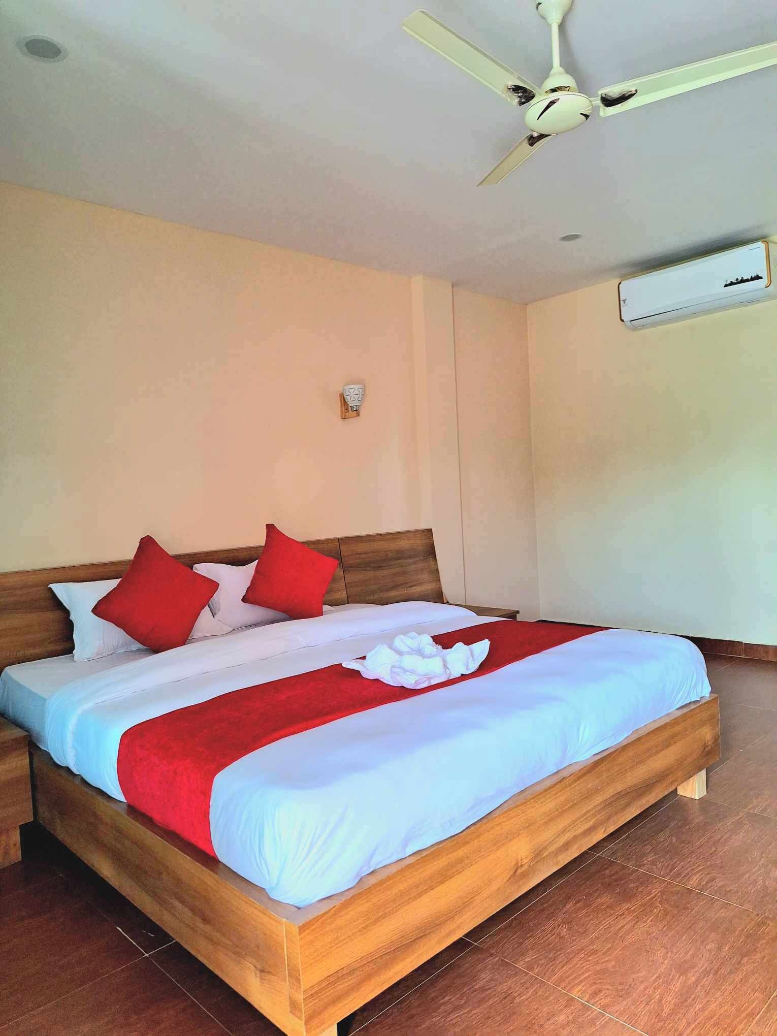 Ein ordentlich bezogenes Bett mit einem hölzernen Kopfteil, einem Deckenventilator und einer Klimaanlage an der Wand.