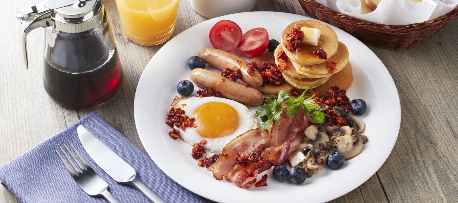A breakfast plate with eggs, bacon, sausages, pancakes, tomatoes, blueberries, and mushrooms.