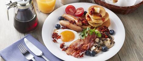 A breakfast plate with eggs, bacon, sausages, pancakes, tomatoes, blueberries, and mushrooms.