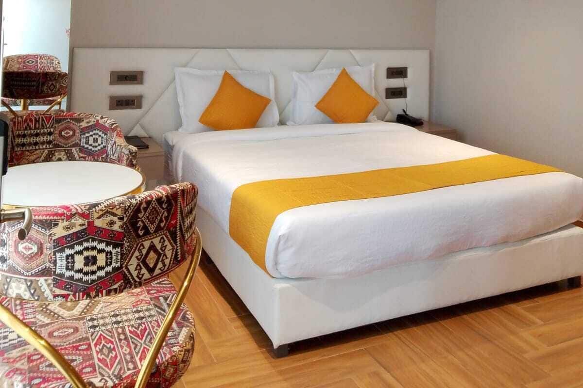 Quarto de hotel moderno com uma cama grande, um ventilador de teto e uma poltrona estampada.
