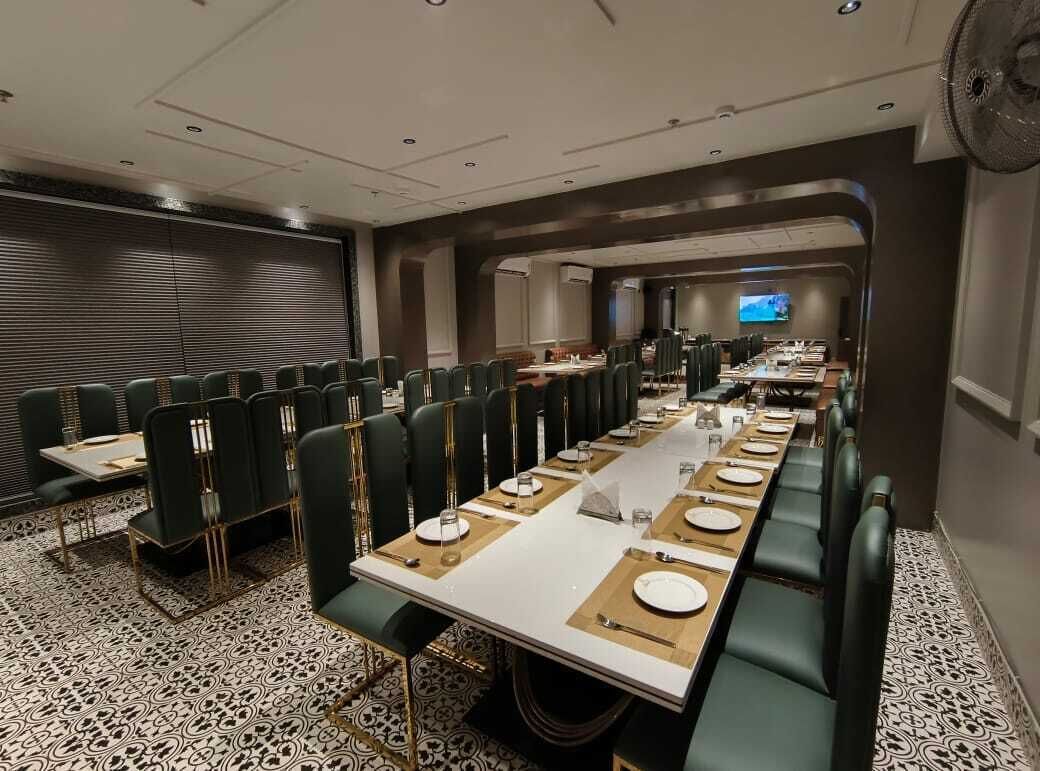 Une salle de conférence avec des rangées de chaises vertes recouvertes de tissu, une longue table préparée pour une réunion et un grand écran à l’avant.