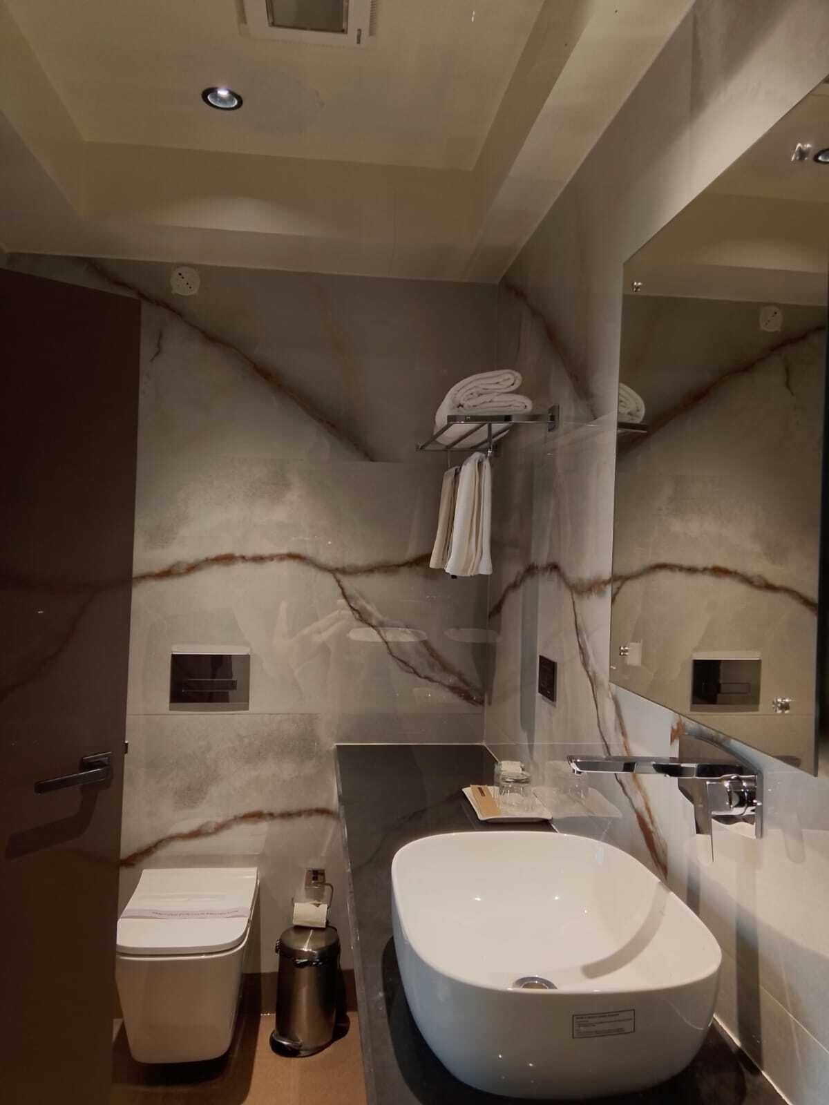 Un baño moderno con pared de mármol, un lavamanos grande y un inodoro.