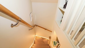 A staircase with wooden handrails, carpeted steps, and a wall-mounted shelf with books and a vase.