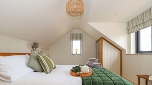 A bedroom with a large bed, a green quilt, a wicker tray with items, and a window with curtains.