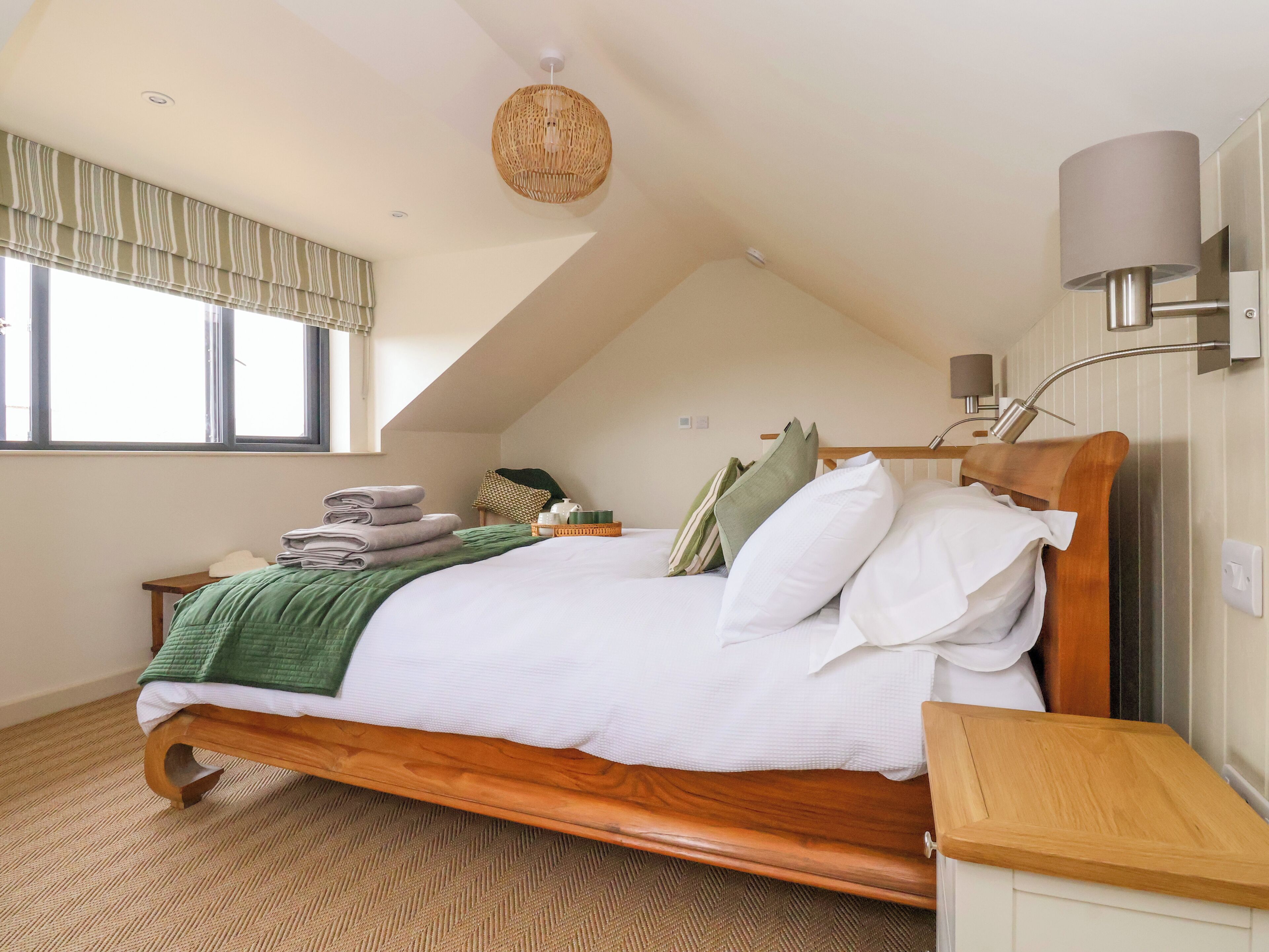 A bedroom with a wooden bed, a green throw blanket, and a bedside table with a lamp.