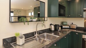 A modern kitchen with a stainless steel sink, green cabinets, a large mirror, and a countertop with various appliances.