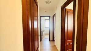Un couloir avec des portes en bois, un sol carrelé et une vue sur une salle de bain équipée de toilettes et d’un lavabo.