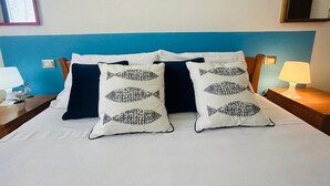 Un lit bien fait, avec deux oreillers ornés d’un motif de poisson, une tête de lit bleue et une table de chevet avec une lampe.