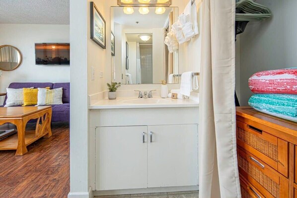 Un bagno con un mobile lavabo bianco, uno specchio e un lavabo. C'è un porta asciugamani sopra lo specchio e un armadietto in legno a destra.