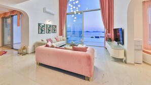 Ein geräumiges Wohnzimmer mit großem Fenster, einem rosafarbenen Sofa und einem Flachbildfernseher.