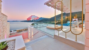 Ein Balkon mit Glasgeländer, der einen Pool und eine Berglandschaft überblickt.