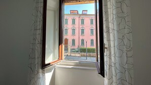 A narrow corridor with a window leading to a pink building with green shutters. - Suite at the foot of the Upper Town (Bergamo)