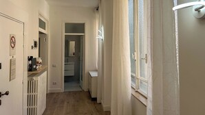 Un pasillo con un radiador, una puerta con un cartel y una ventana con cortinas.