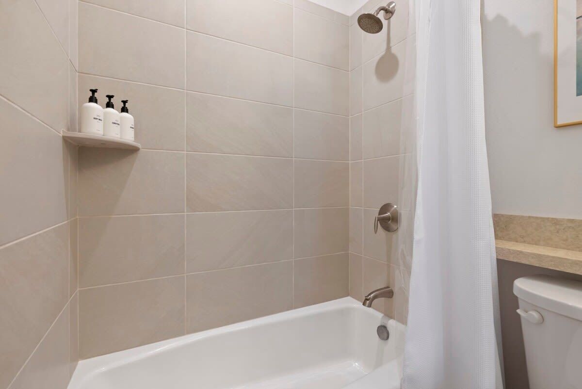 A bathroom with a bathtub, a shower, and a toilet. There are toiletries on a shelf.