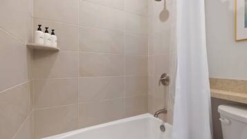 A bathroom with a bathtub, a shower, and a toilet. There are toiletries on a shelf.
