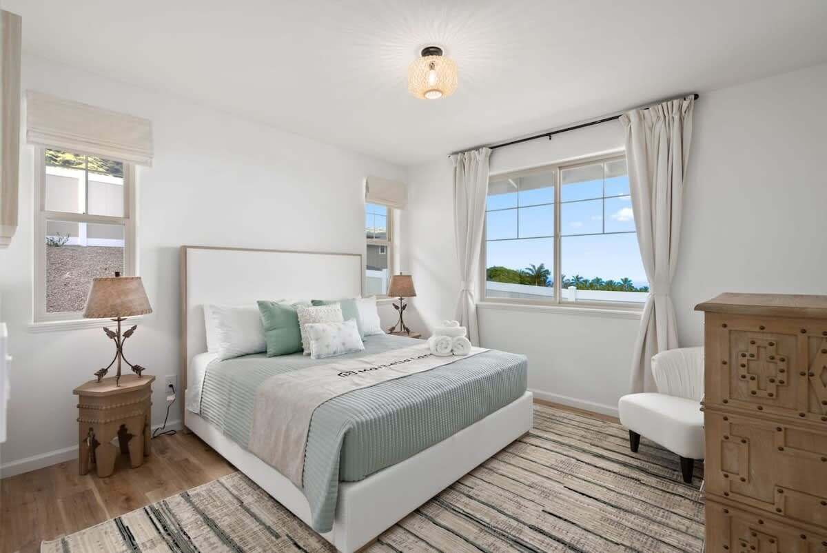 A bedroom with a bed, bedside tables, a dresser, a window with curtains, and a view of the outdoors.