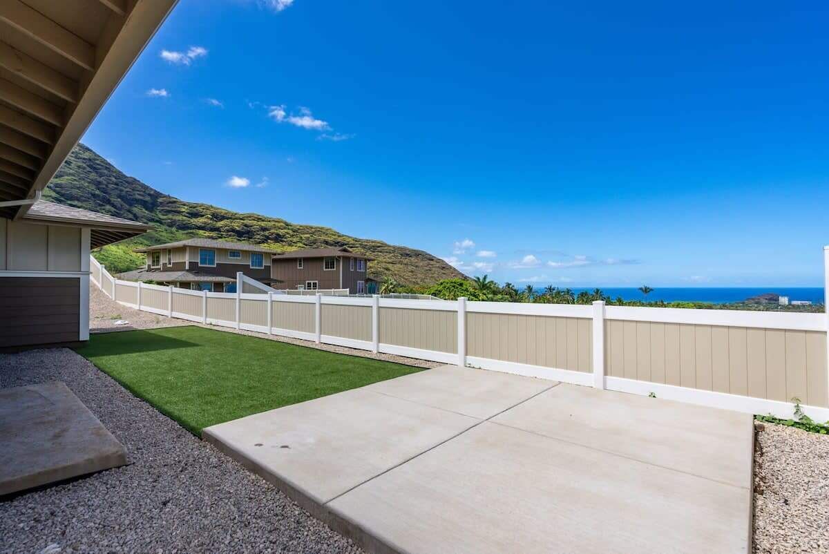 A residential property with a concrete patio, a white fence, and a view of a mountainous landscape and ocean.