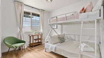 A bunk bed room with a desk and chair, a window with curtains, and a view of the beach.