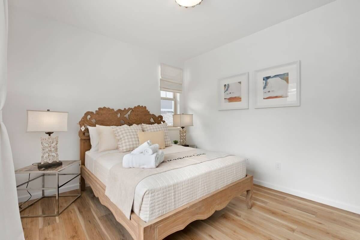 A neatly arranged bedroom with a wooden bed, white bedding, two bedside lamps, and two framed artworks on the wall.