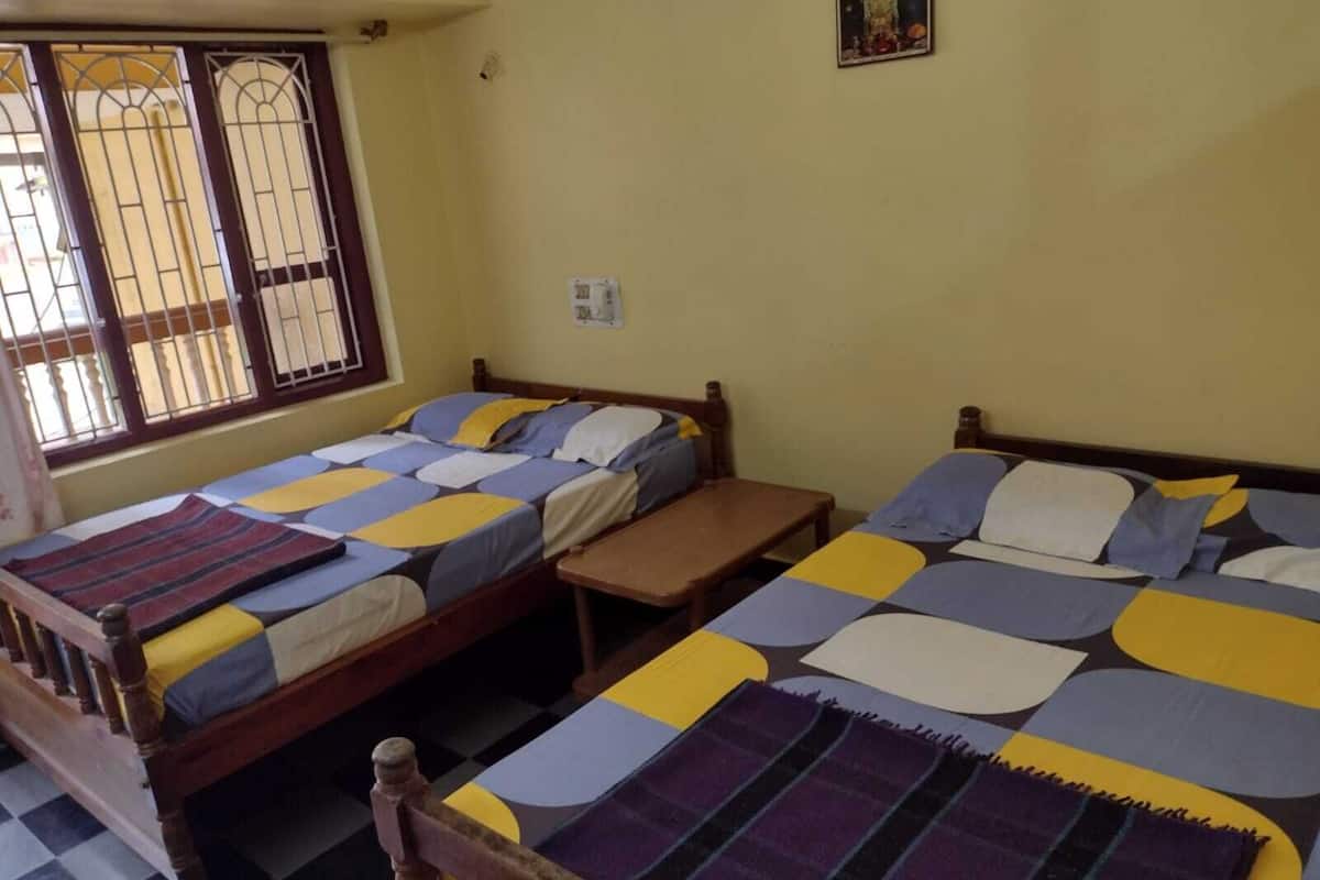 A room with two wooden beds, each with a colorful bedspread. There is a small wooden table between the beds, and a window with metal bars on the left.
