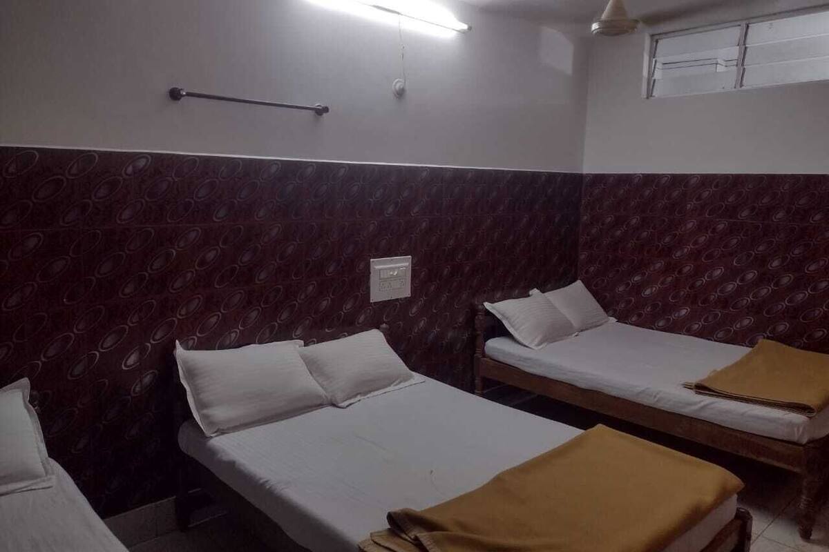A room with two single beds, a wall-mounted light fixture, a ceiling fan, and a window with a view of the outside.