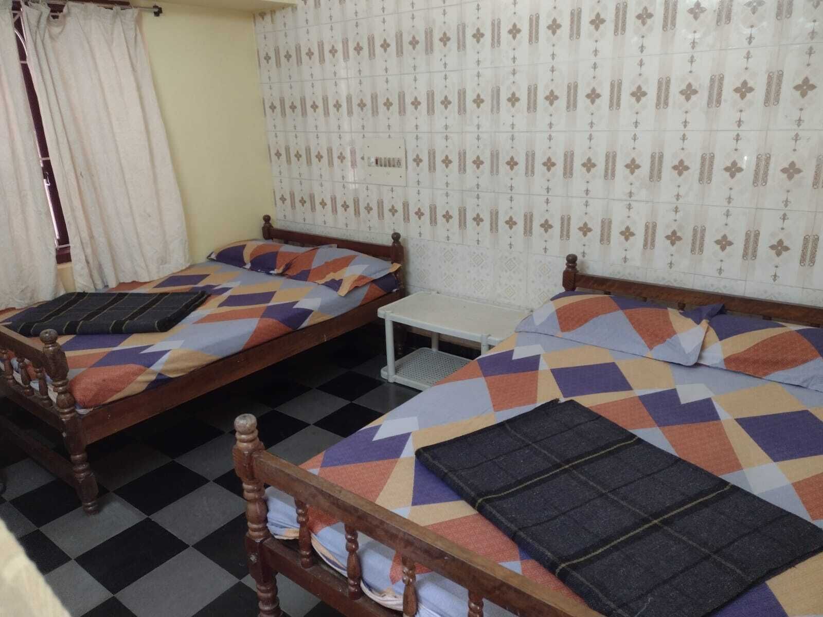 A room with two wooden beds, each with a patterned bedspread and pillows. There is a small white table between the beds.