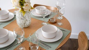 A dining table set with white plates, bowls, and clear wine glasses, accompanied by a vase of white flowers. - Manchester - Apartment - Sleeps 5 - Parking (Salford)