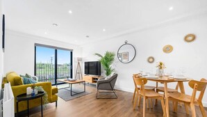 A modern living room with a sofa, a dining table set for four, a TV, and a large window with a view. - Manchester - Apartment - Sleeps 5 - Parking (Salford)