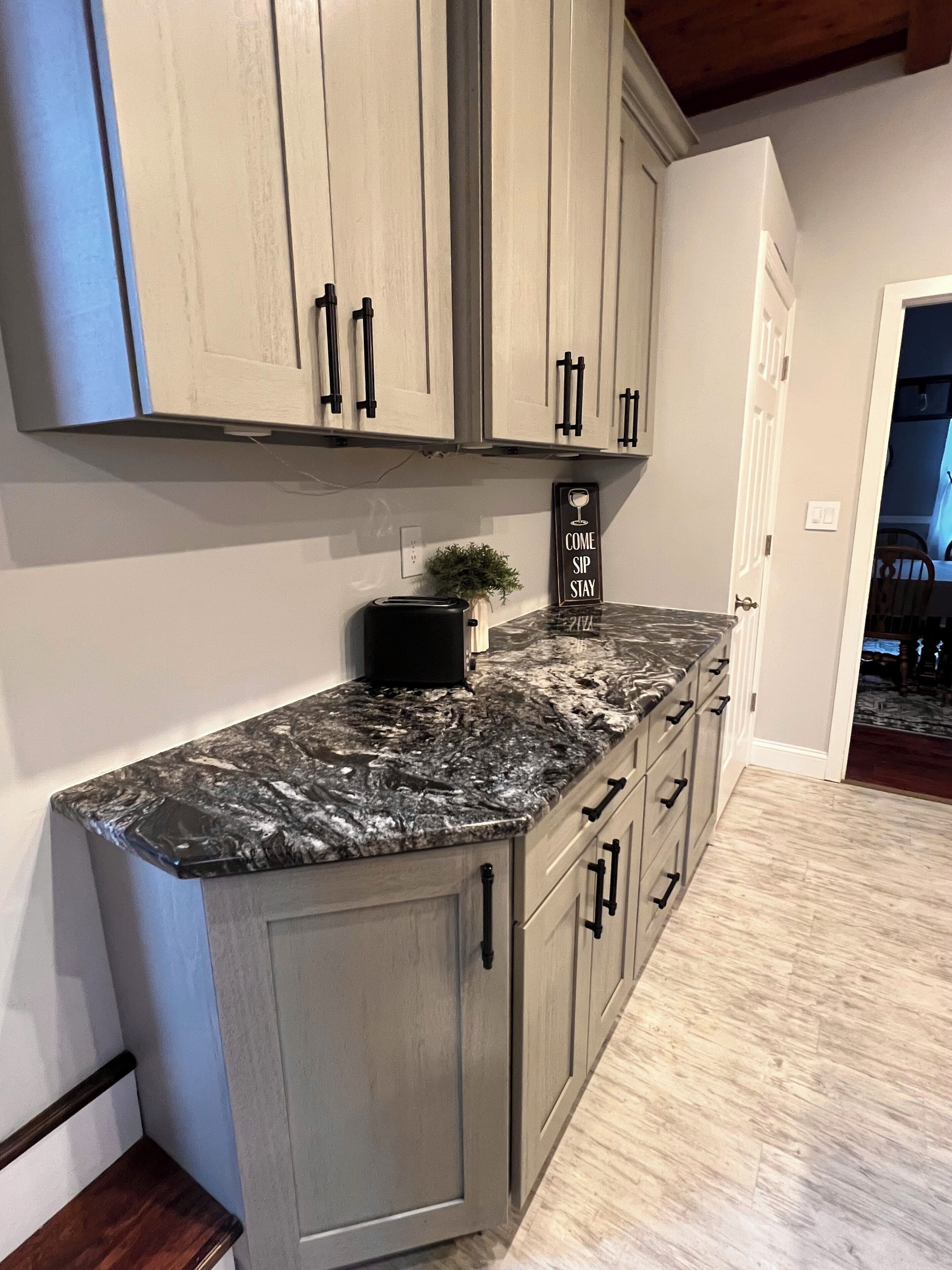 A kitchen with light gray cabinets, a black marble countertop, and a small potted plant.