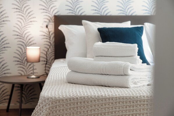A neatly made bed with white and blue pillows, a white textured blanket, and a stack of white towels.