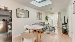 A modern living room with a sofa, two chairs, a small table, a TV, and a kitchen area with a fridge. - @ Marbella Lane -cozy 1BR Studio in Palo Alto Dwtn (Palo Alto)